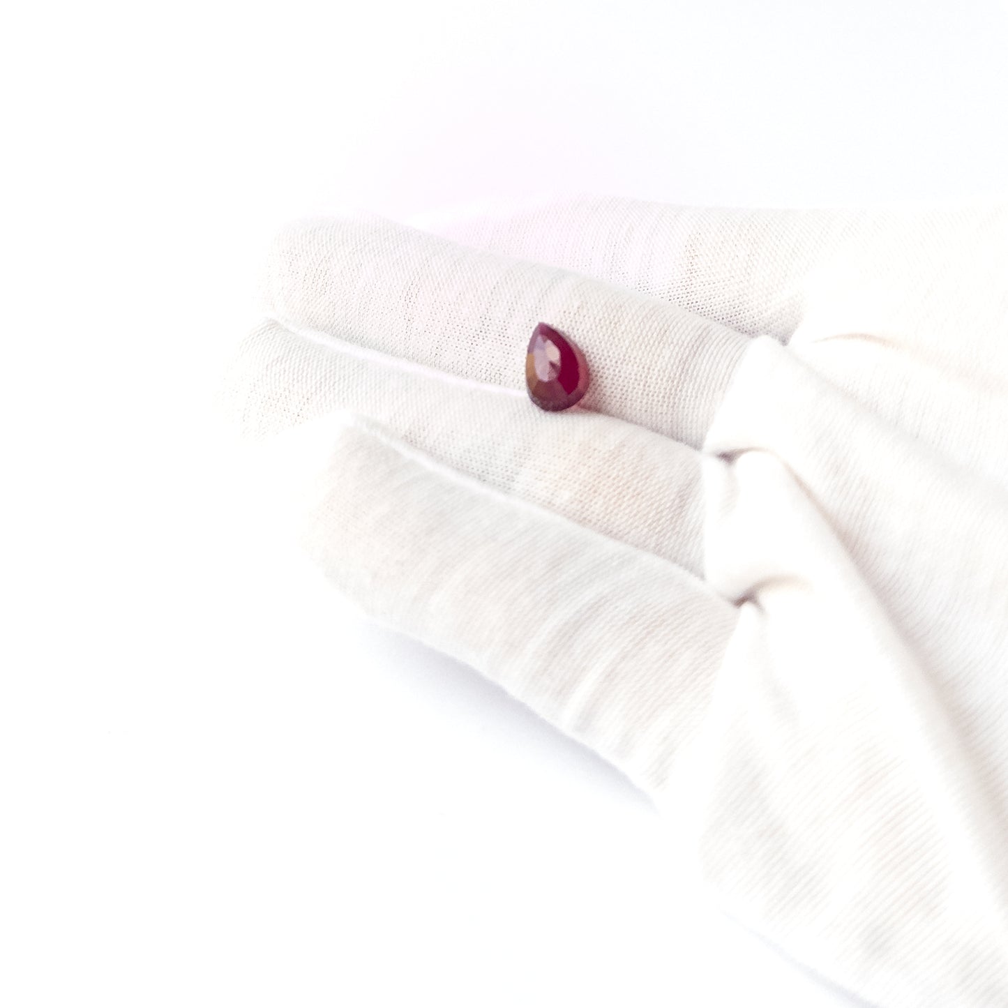 A person holds delicate pieces of Ruby cabochon, showcasing their pear‑cut design.