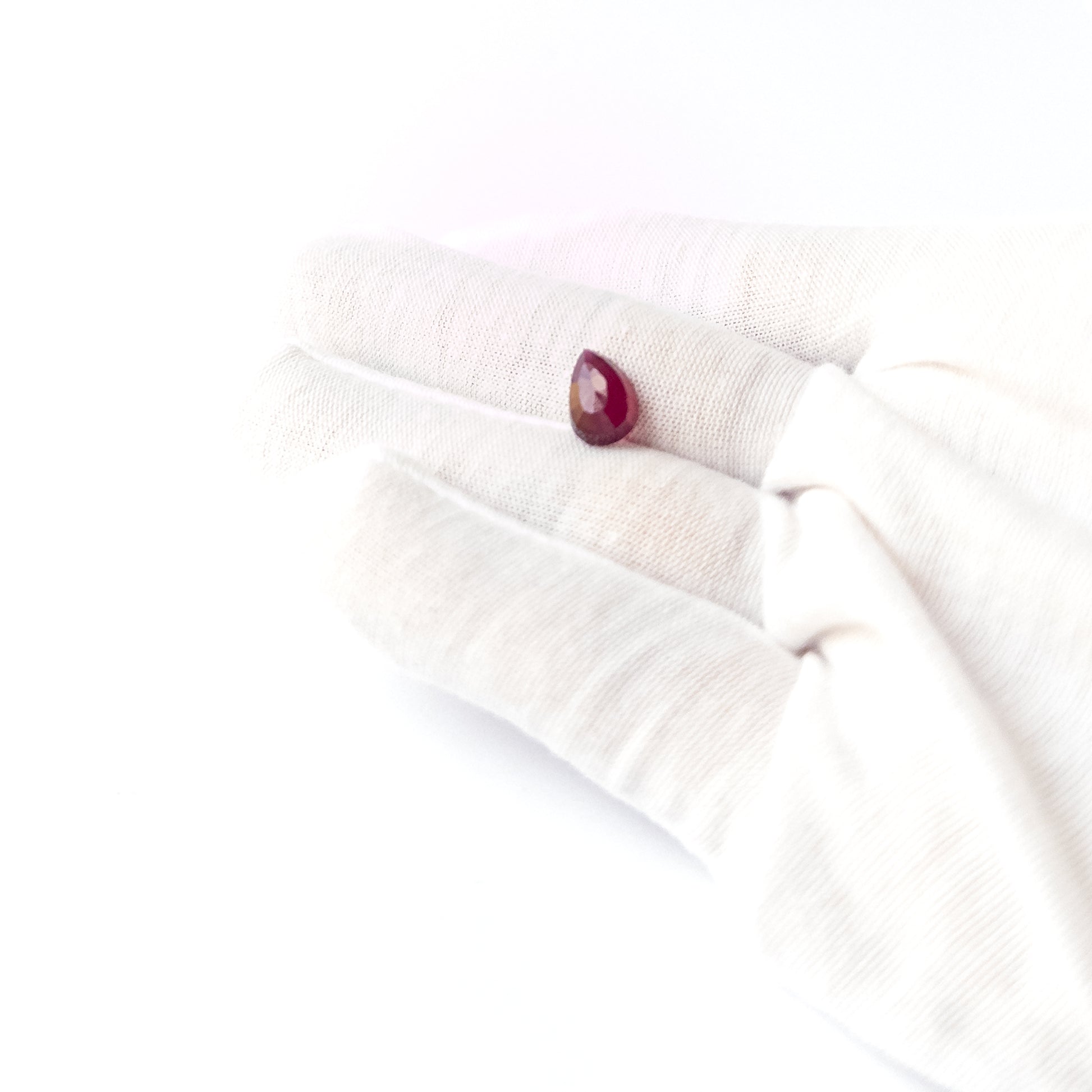 A person holds delicate pieces of Ruby cabochon, showcasing their pear‑cut design.