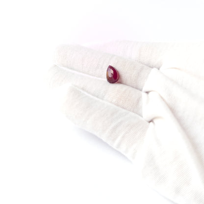 A person holds delicate pieces of Ruby cabochon, showcasing their pear‑cut design.