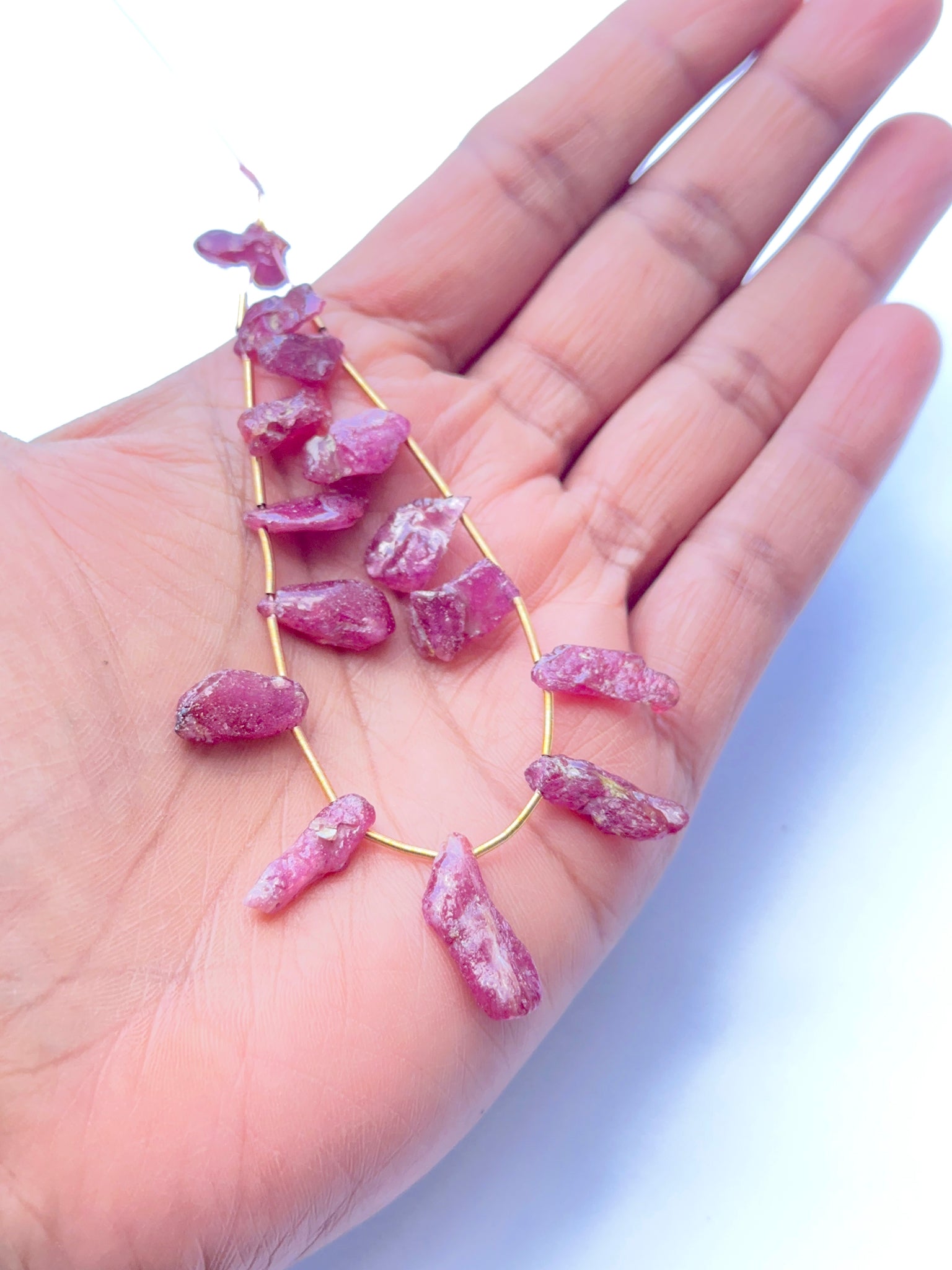 A person holds delicate strands of ruby rough beads, showcasing their smooth design