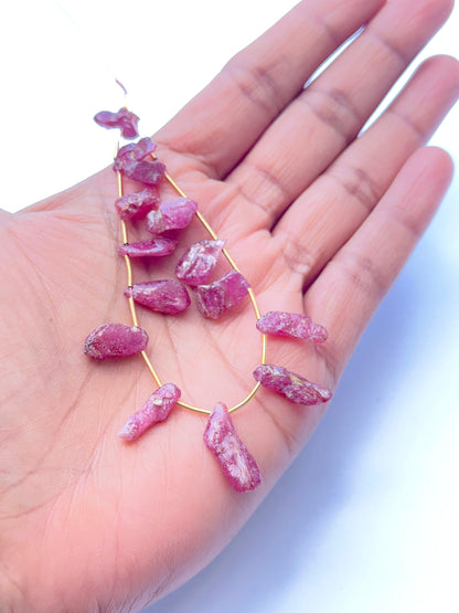 A person holds delicate strands of ruby rough beads, showcasing their smooth design