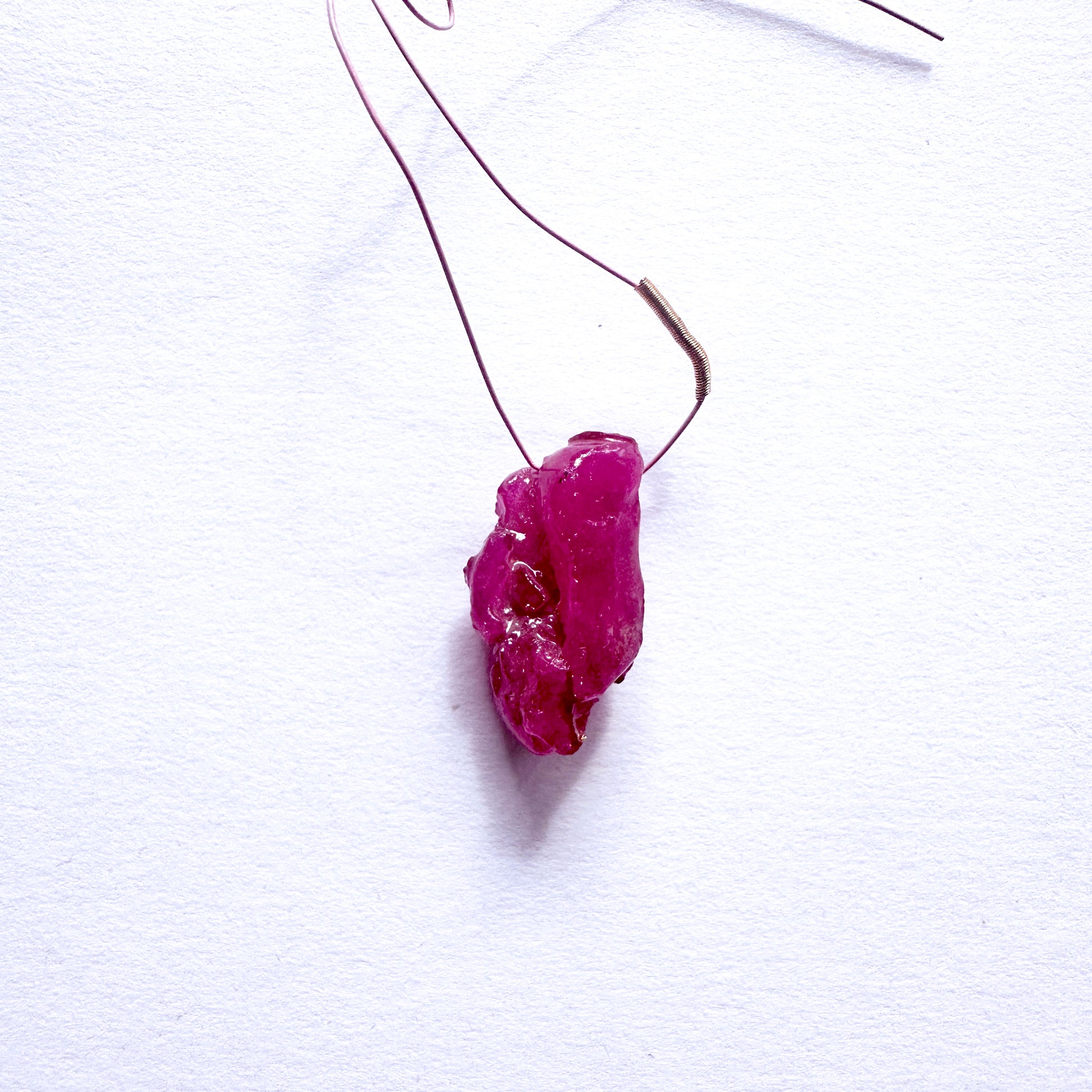 A stunning 17-carat red ruby drilled rough, elegantly hung from a delicate wire tassel.