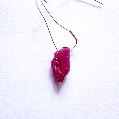 A stunning 17-carat red ruby drilled rough, elegantly hung from a delicate wire tassel.
