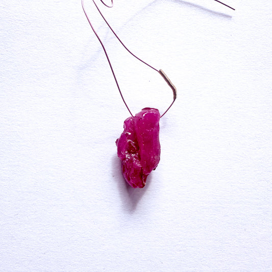 A stunning 17-carat red ruby drilled rough, elegantly hung from a delicate wire tassel.