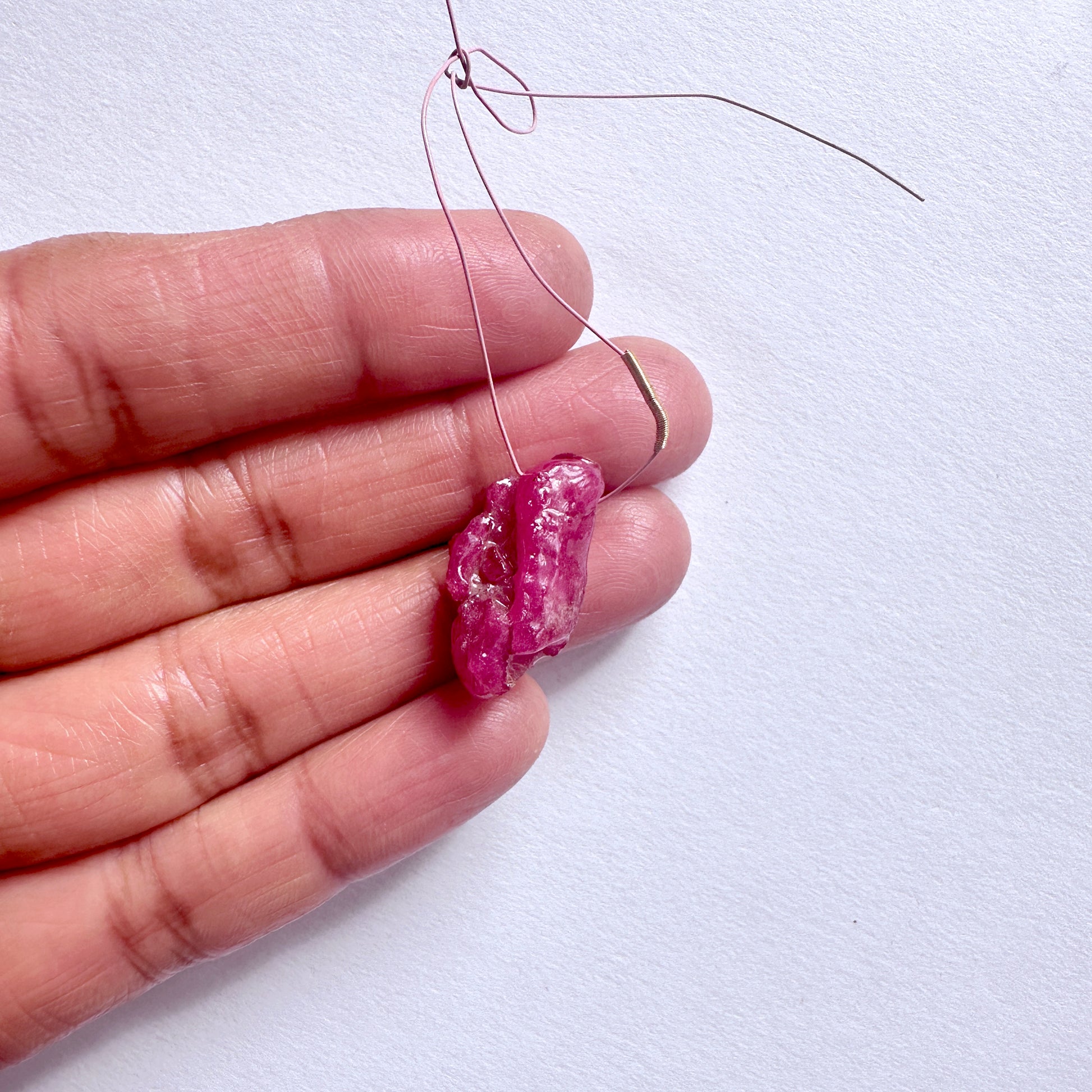 Ruby rough beadon a wire held between fingers against a white background