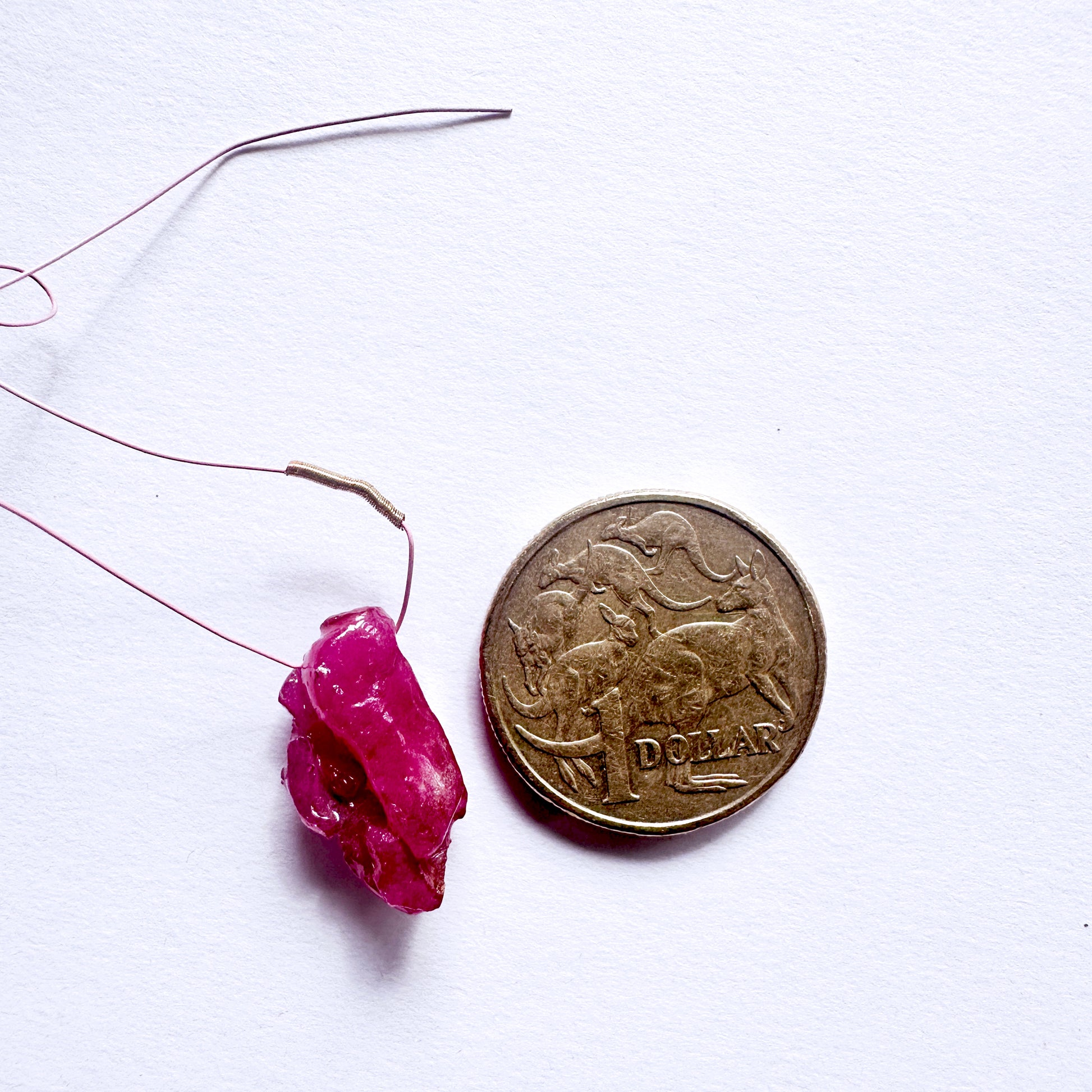 Pink Ruby rough bead on a string next to a coin on a white background