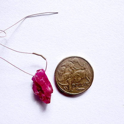 Pink Ruby rough bead on a string next to a coin on a white background