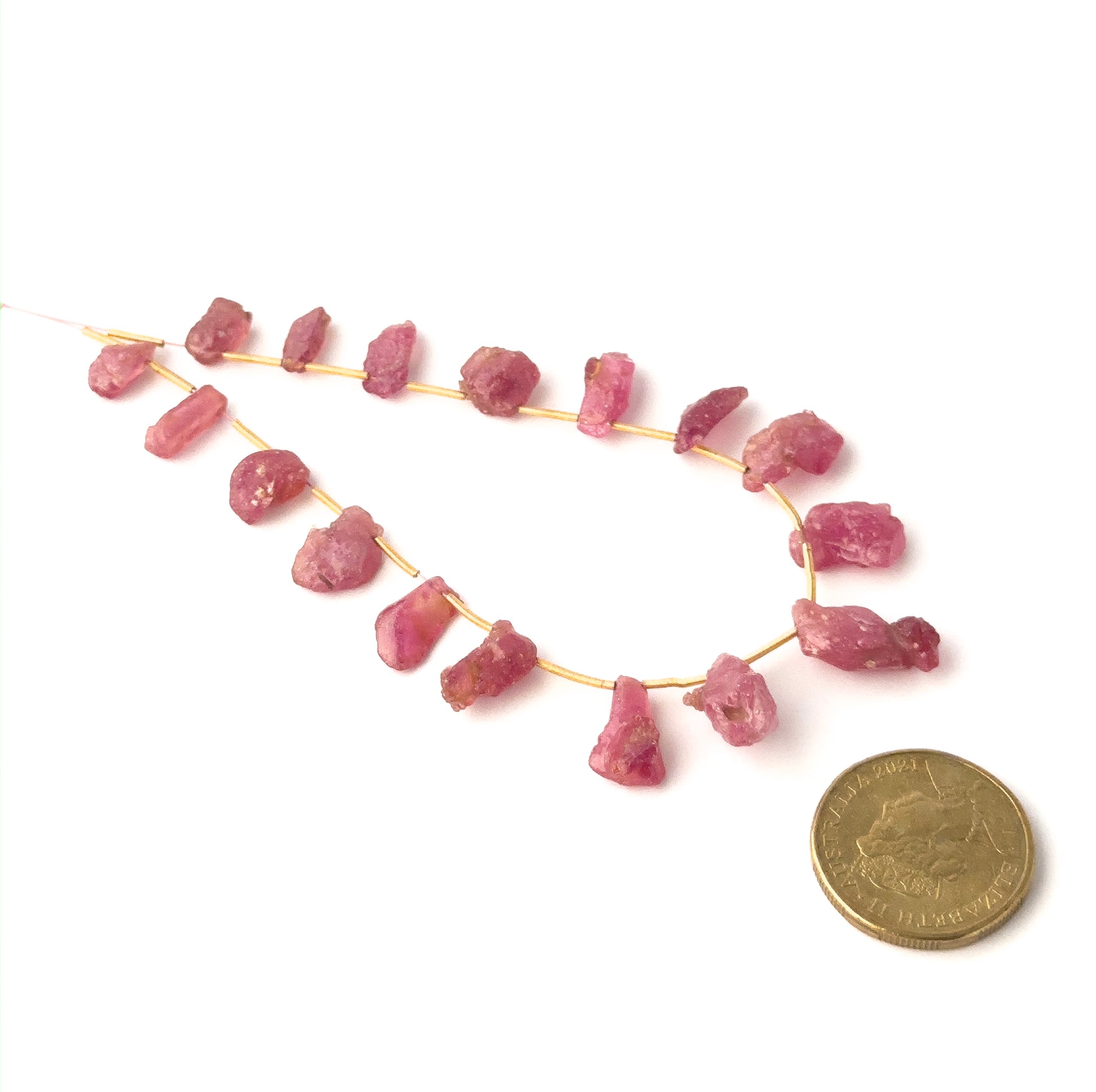 A coin is placed near delicate Ruby rough pieces for scale.