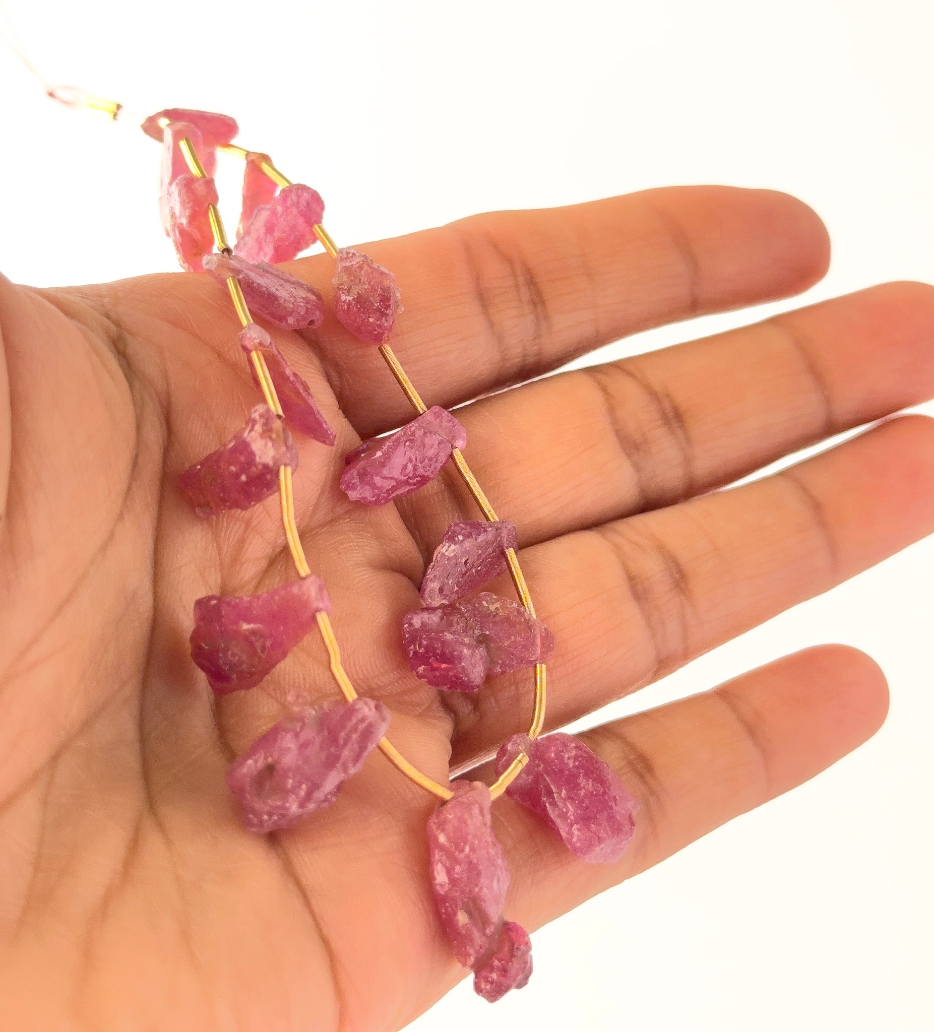 A person holds delicate strands of Ruby rough pieces, showcasing their side‑drilled design.