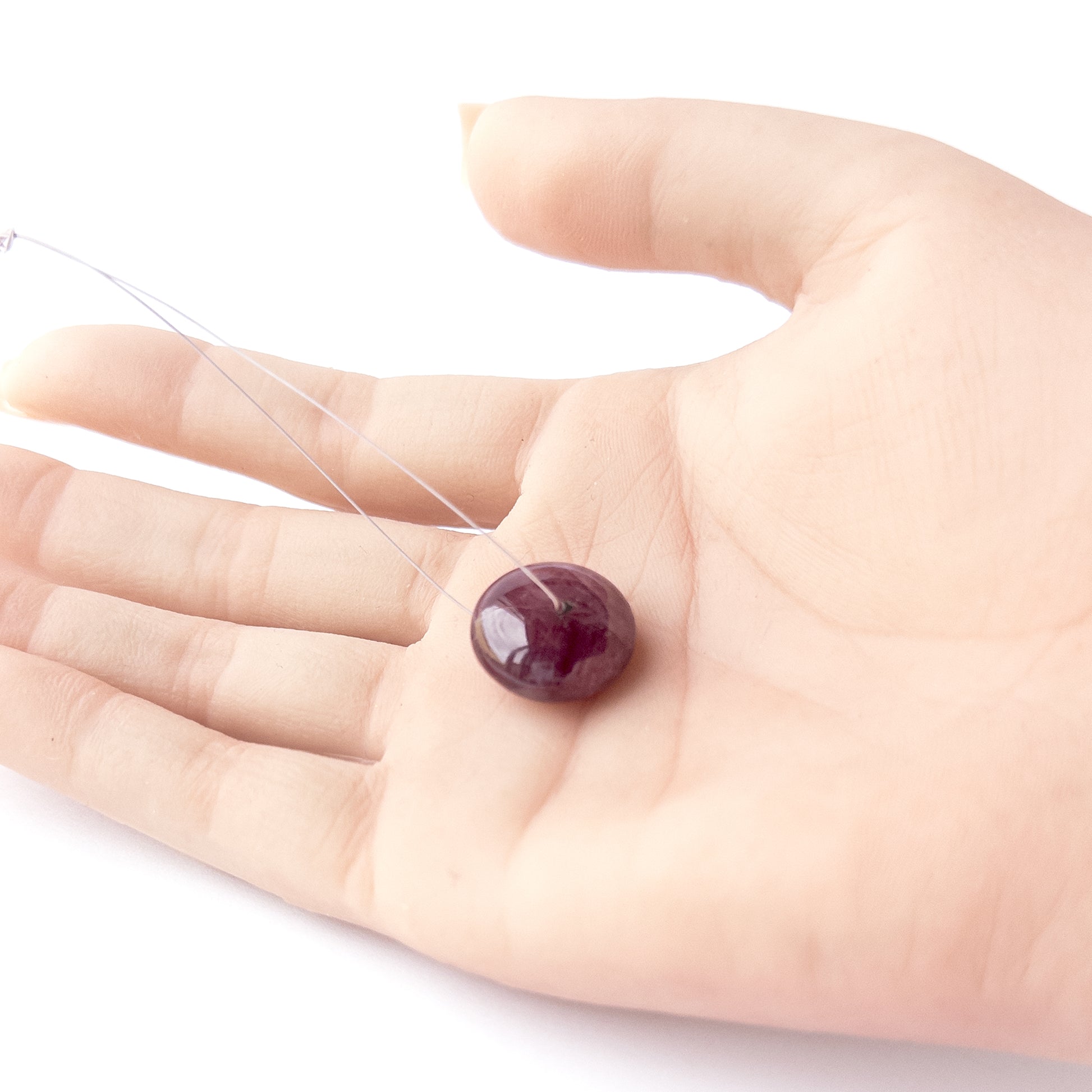 A person holds delicate pieces of Ruby beads, showcasing their smooth disc design.