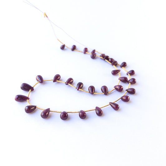 Handmade jewellery components with natural ruby smooth drop beads arranged in a 22‑piece set.