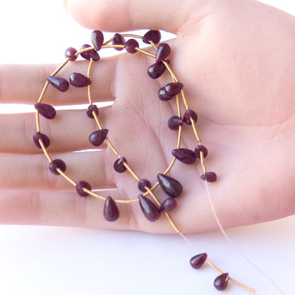 A person holds delicate pieces of Ruby beads, showcasing their smooth drop design.