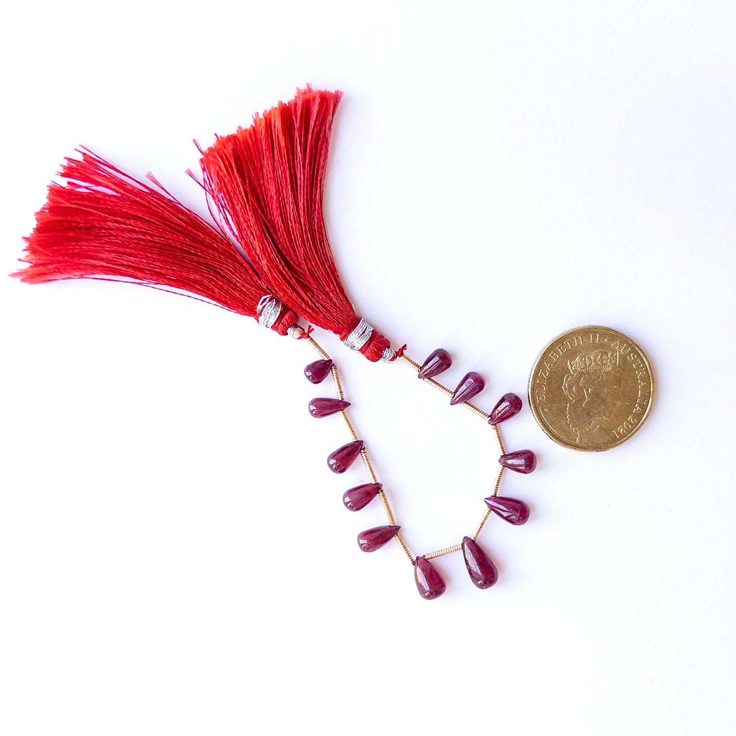 A coin is place near delicate strands of Ruby beads for scale.