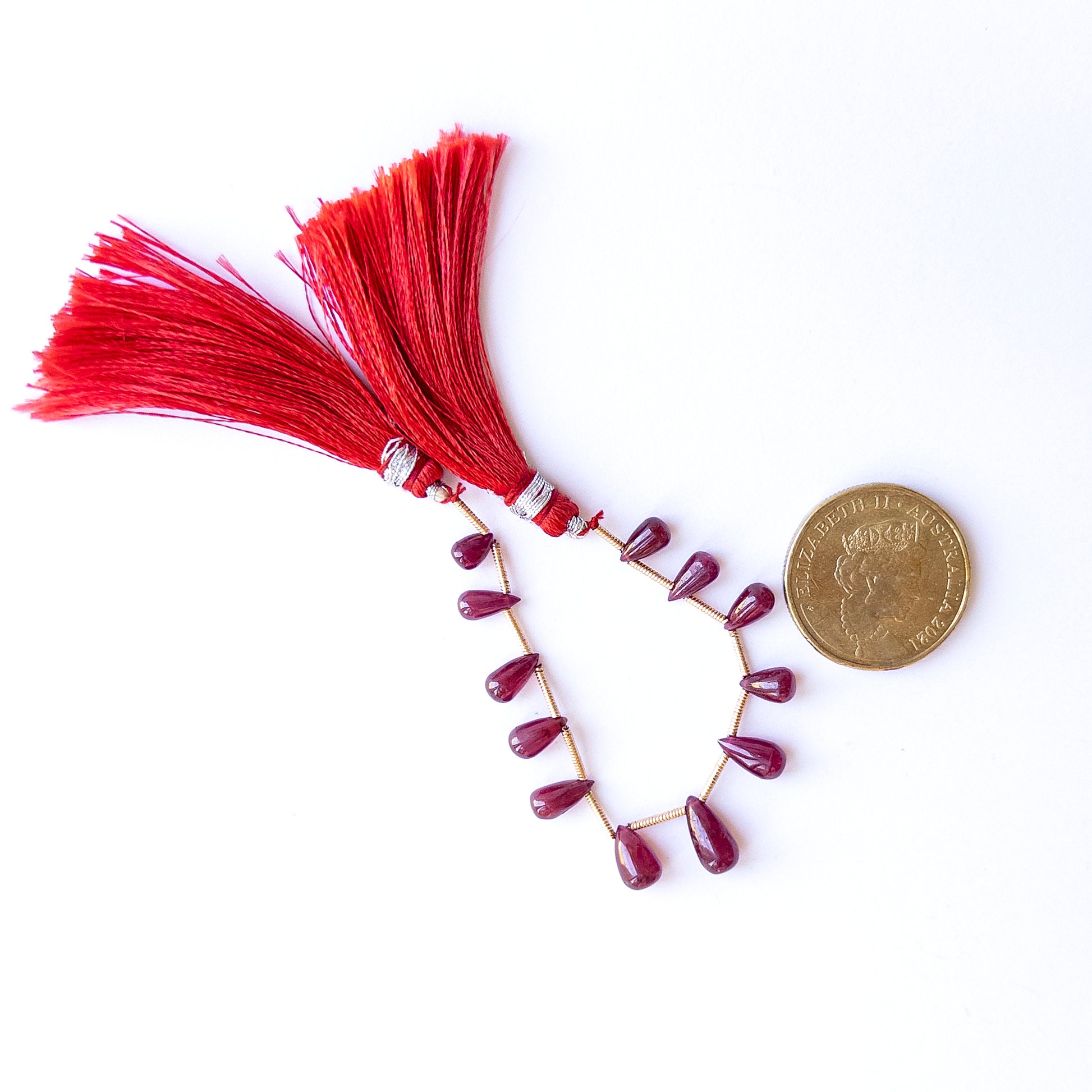 A coin is place near delicate strands of Ruby beads for scale.