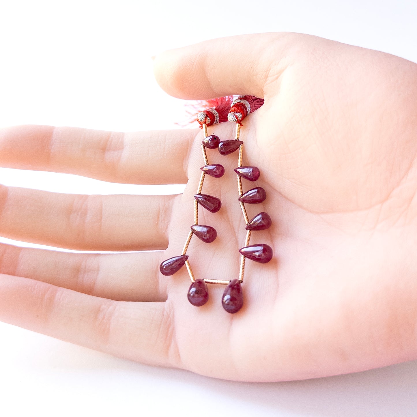 A person holds delicate strands of Ruby beads, showcasing their smooth drop design.