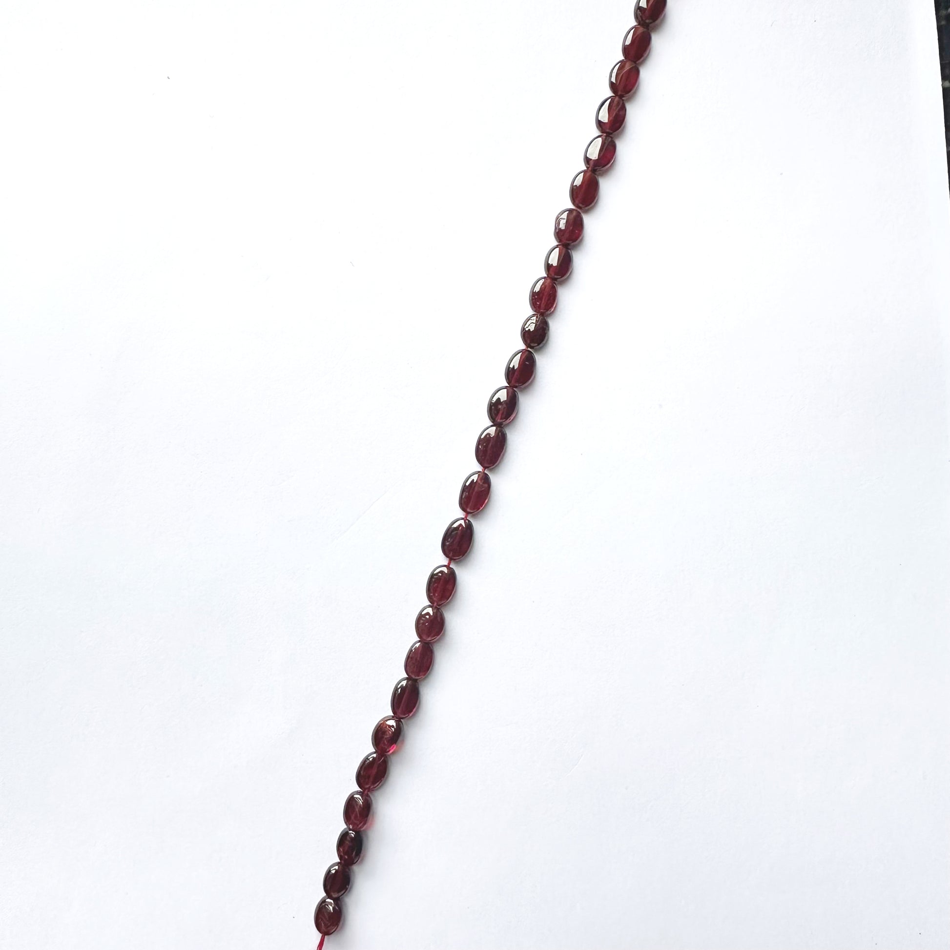Close-up of Ruby beads arranged in a 20cm strand with glossy surface and rich hue.