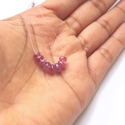 A person holds delicate strands of ruby beads, showcasing their smooth design.