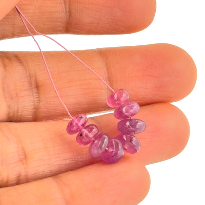 A person holds delicate Ruby beads, showcasing their smooth rondelle design.