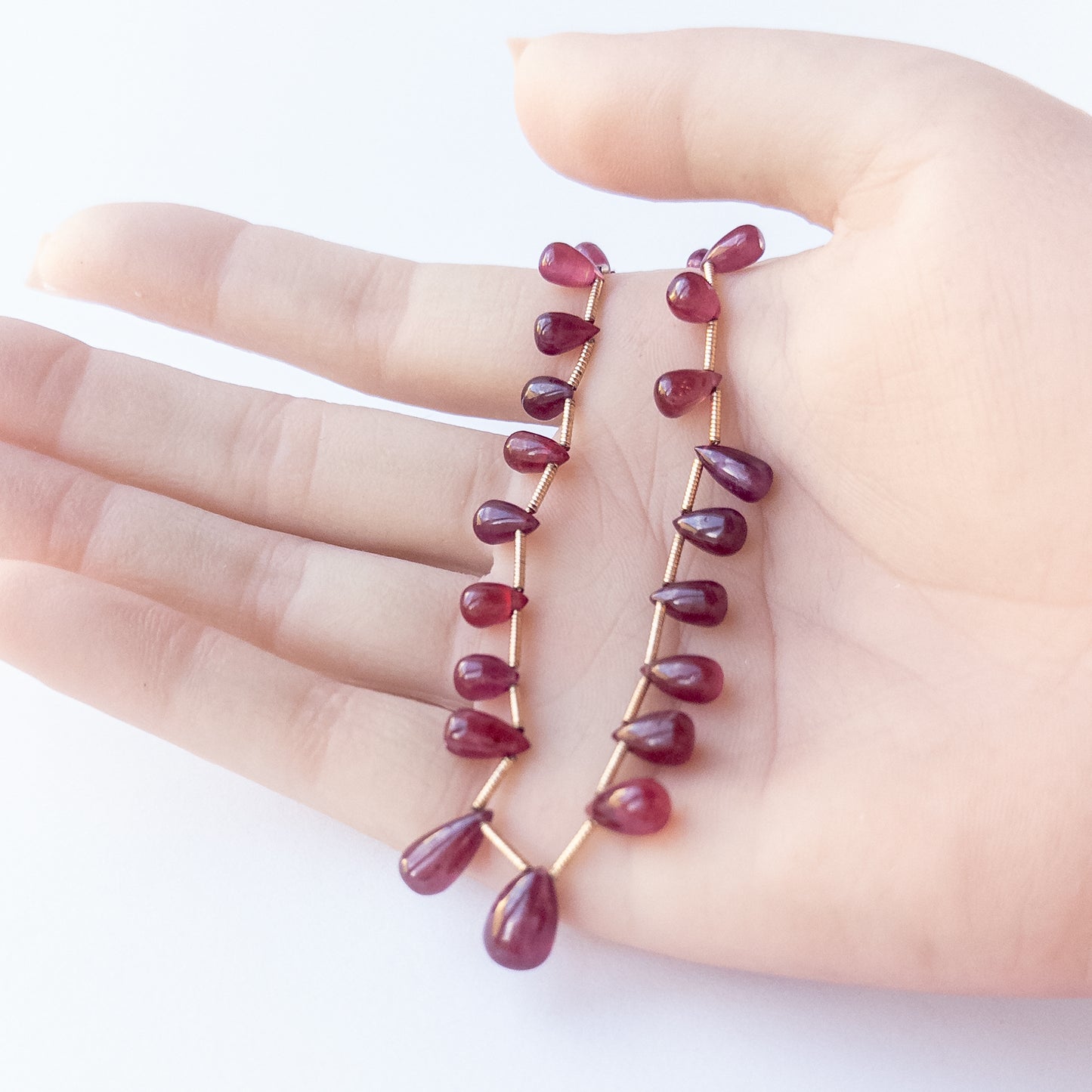 A person holds Ruby briolette pieces, showcasing their smooth teardrop design and size variation.  