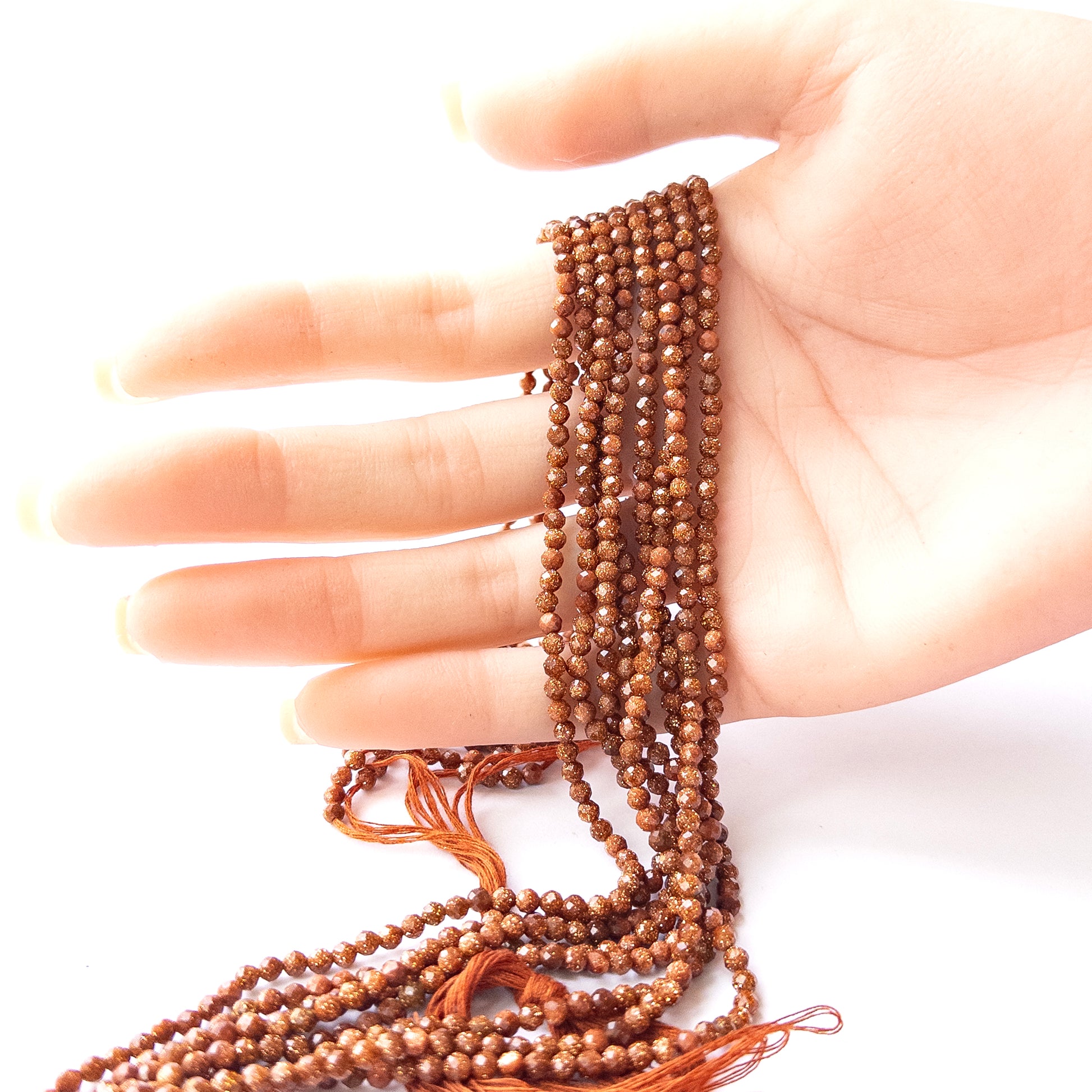 A person holds delicate strands of Sandstone beads, showcasing their faceted rondelle design.