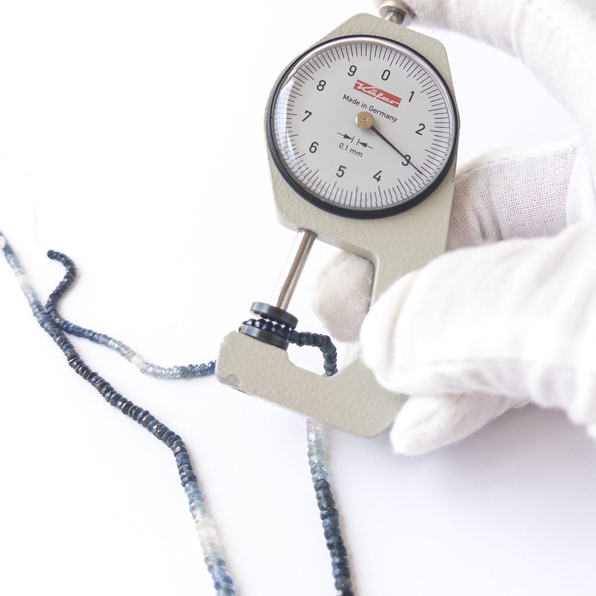 A dial gauge measures the Blue Sapphire faceted rondelle 2.6–3.5mm gemstone.