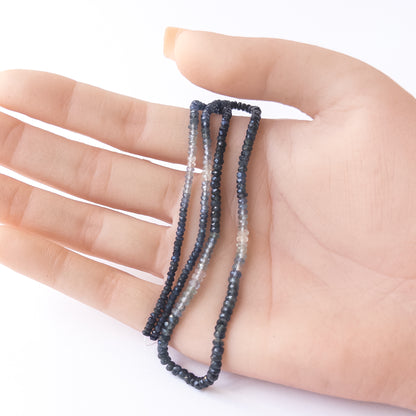 A person holds delicate strands of Blue Sapphire beads, showcasing their faceted rondelle design.