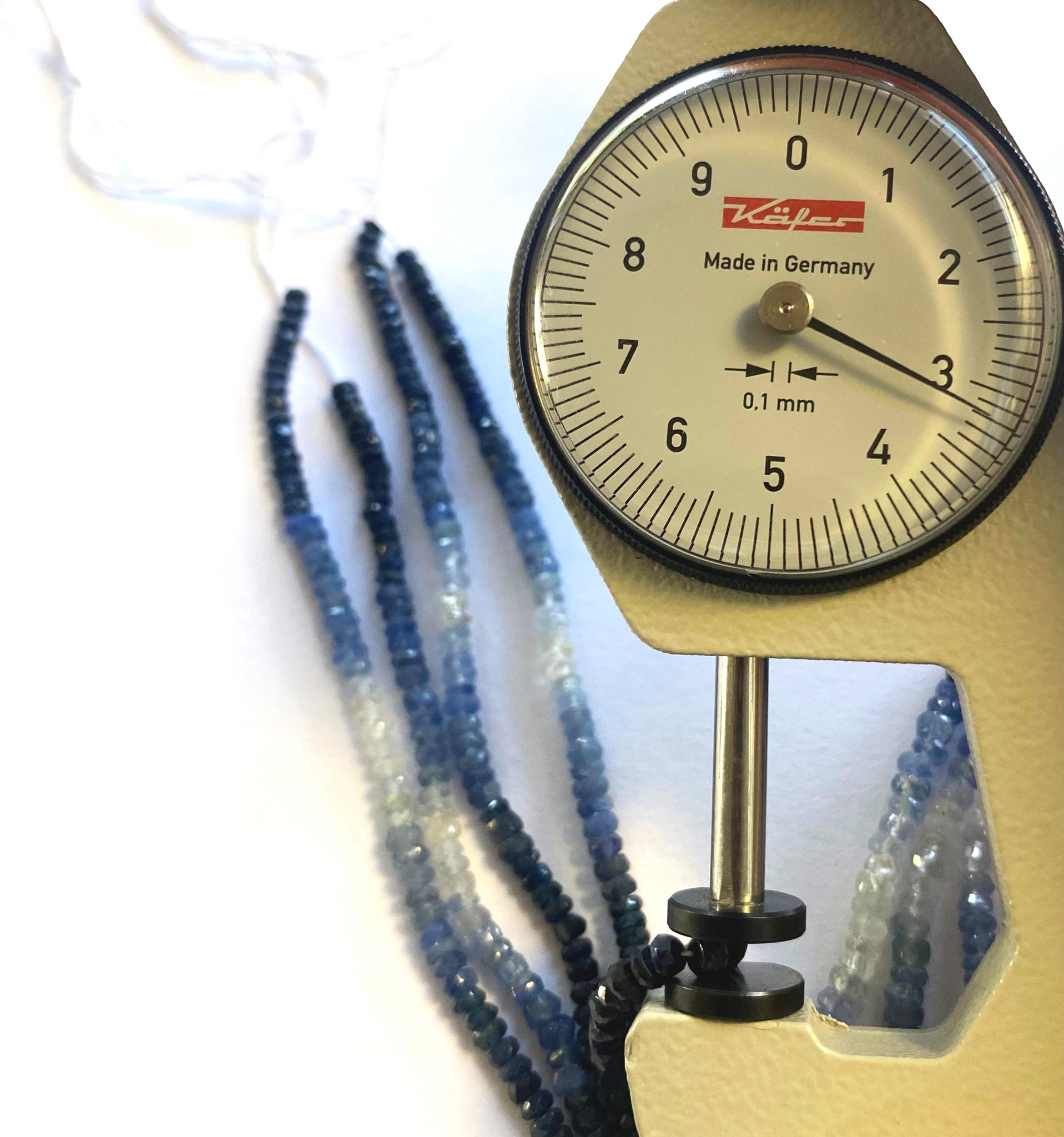 A dial gauge measures the Blue Sapphire faceted rondelle 2.8–3.5mm gemstone for sizing precision.