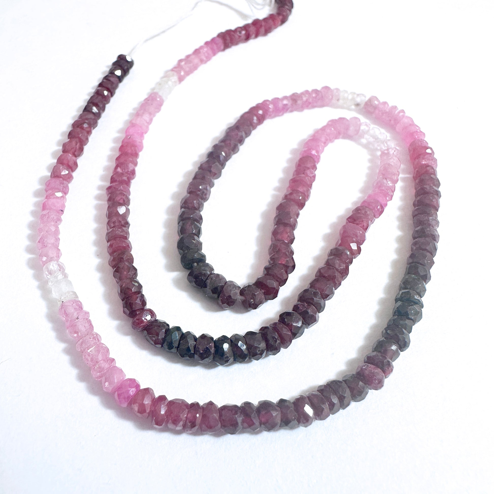 Ruby gemstone beads with faceted rondelle shape reflect light beautifully on a white background.