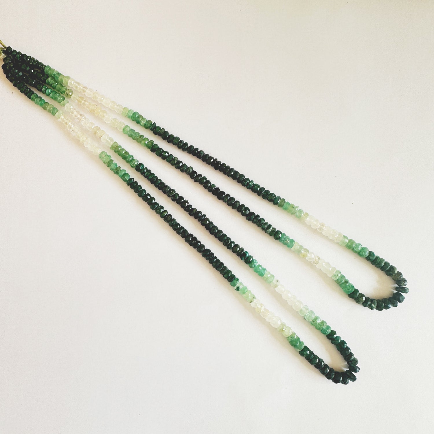 Faceted Emerald rondelle beads in 3.6–5.0mm sizes with shaded green hues and polished sparkle.