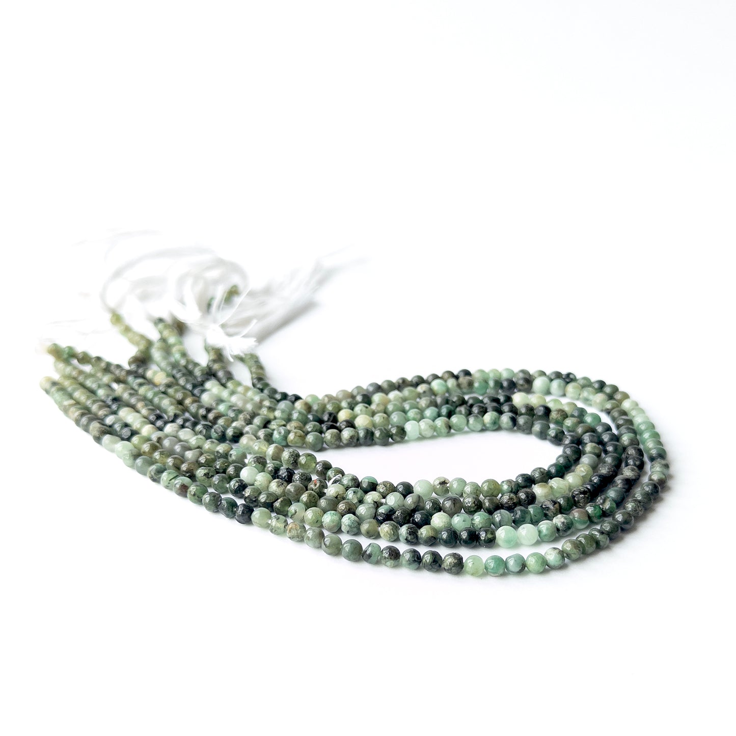 Close‑up of Shaded Emerald smooth round beads highlighting natural colour variation, polish, and quality for DIY jewellery making.