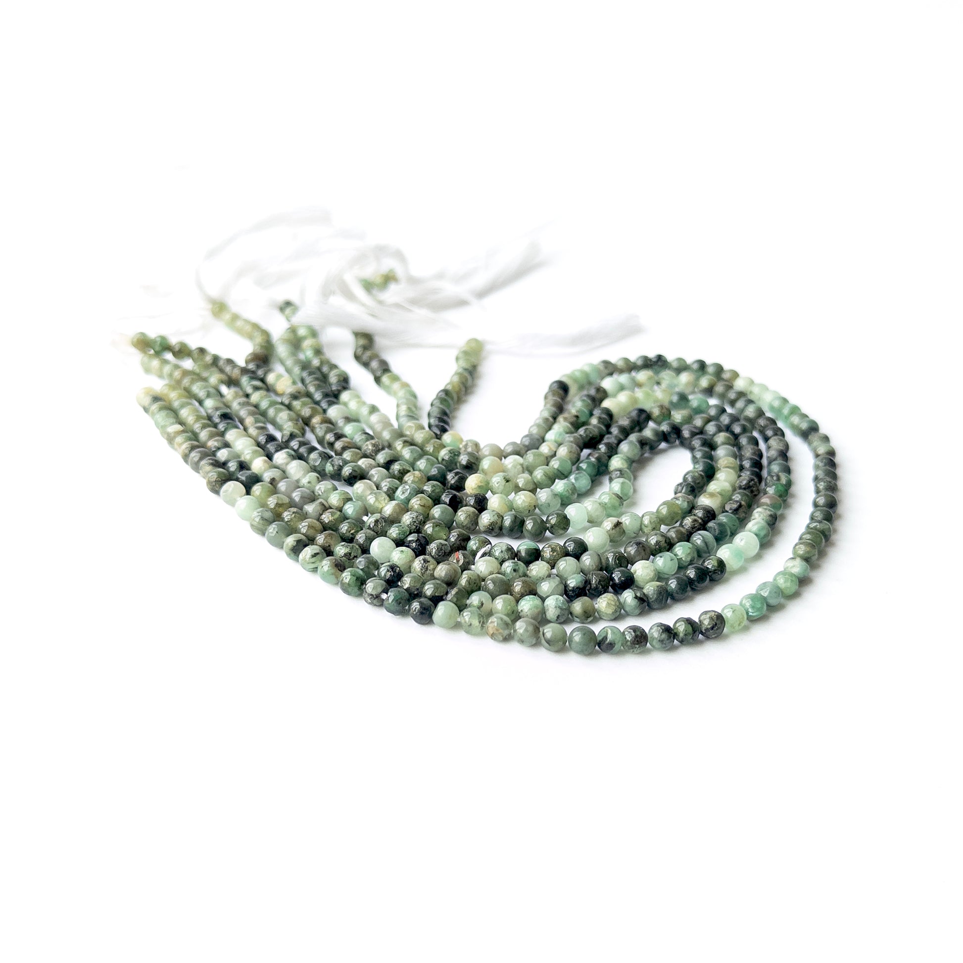 Strands of Shaded Emerald smooth round gemstone beads arranged neatly, showcasing their smooth finish and rich green hues.