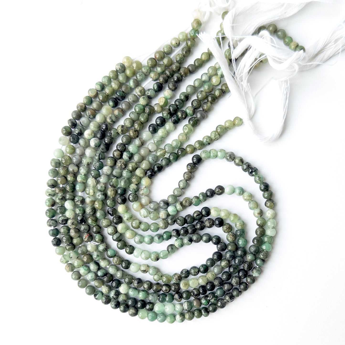 Shaded Emerald smooth round beads displayed in multiple strands, showing consistent sizing and natural variation.