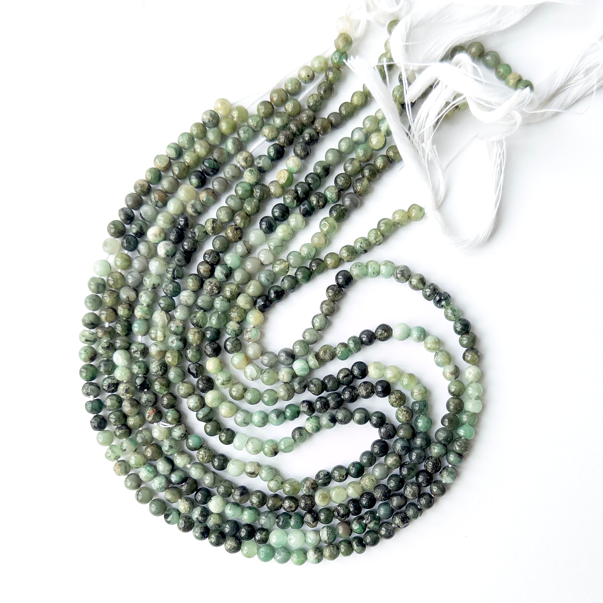 Shaded Emerald smooth round beads displayed in multiple strands, showing consistent sizing and natural variation.