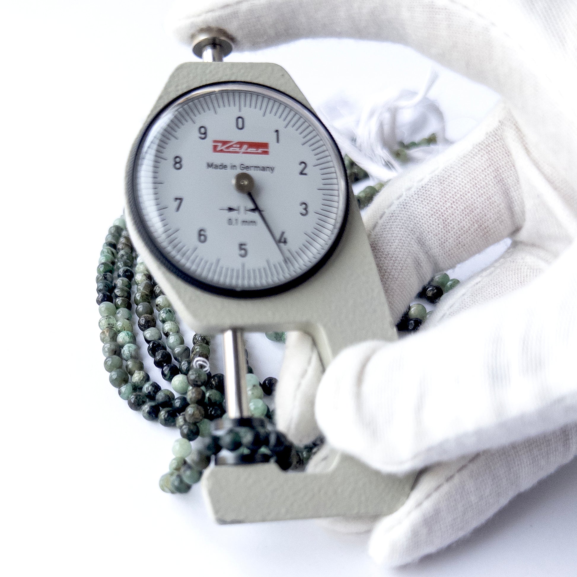 A dial gauge measures the Shaded Emerald smooth round 4–4.2mm gemstone bead.