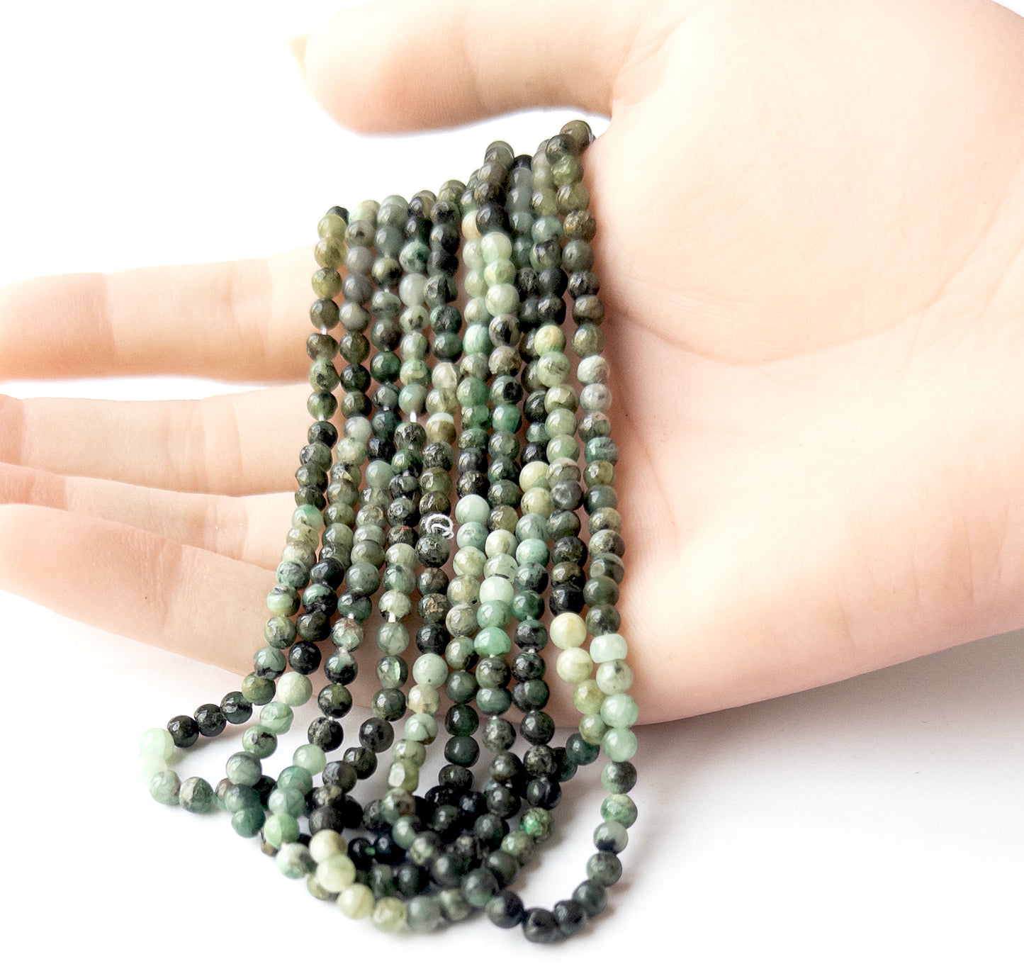 A person holds delicate strands of Shaded Emerald beads, showcasing their smooth round design.