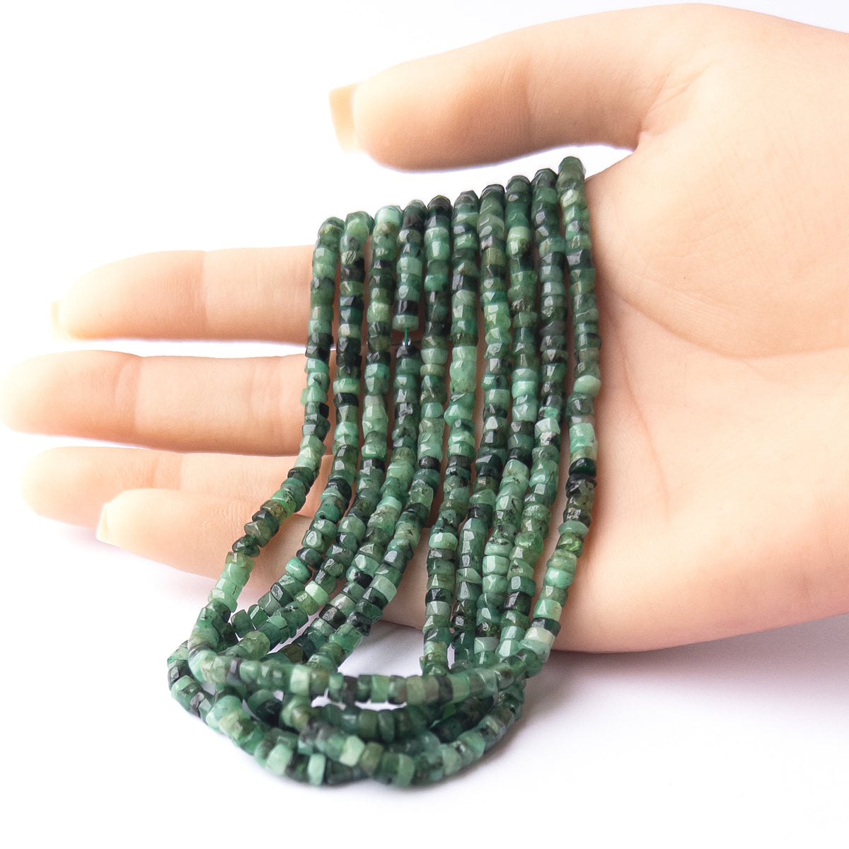A person holds delicate strands of Shaded Emerald beads, showcasing their smooth wheel Heishi design.