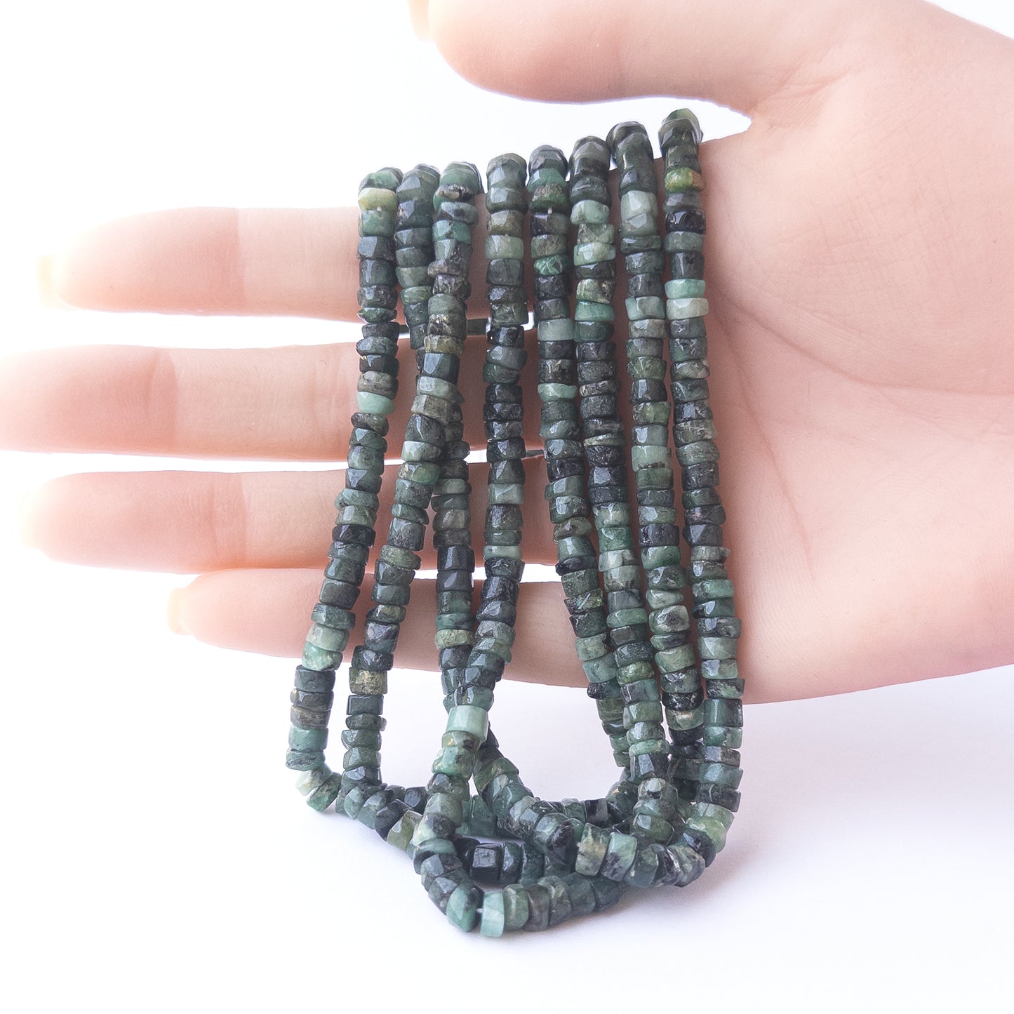 A person holds delicate strands of Shaded Emerald smooth wheel beads, showcasing their polished design.