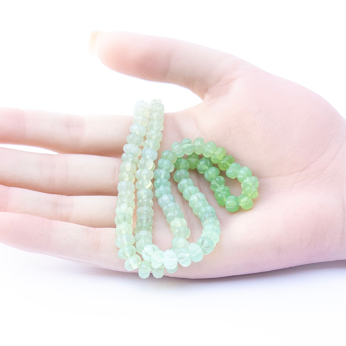 A person holds delicate strands of Shaded Green Chalcedony beads, showcasing their pumpkin cut design.