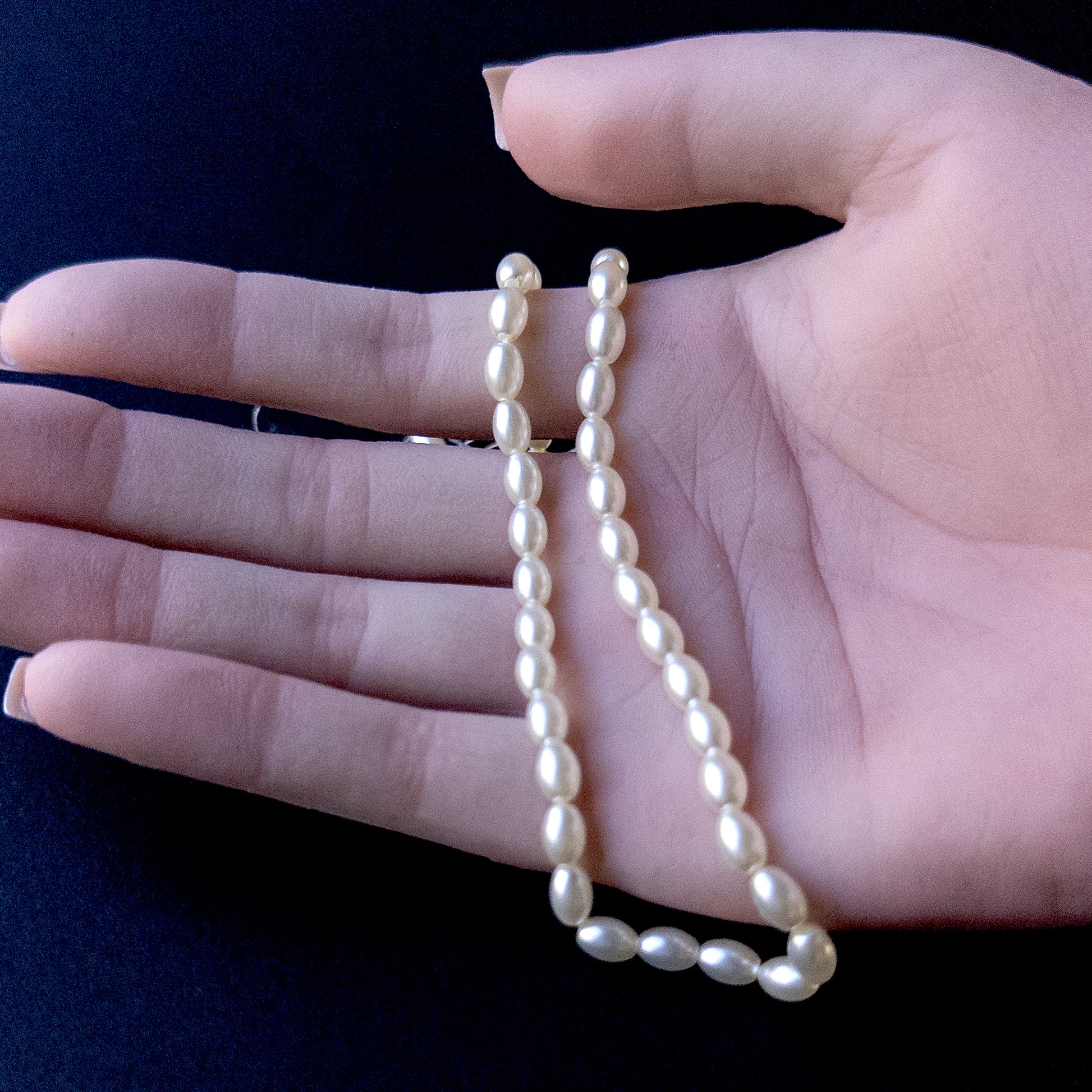 A person holds delicate strands of Shell Pearl smooth oval beads, showcasing their polished design.