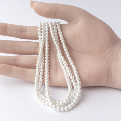 A person holds delicate strands of Shell Pearl beads, showcasing their smooth round design.