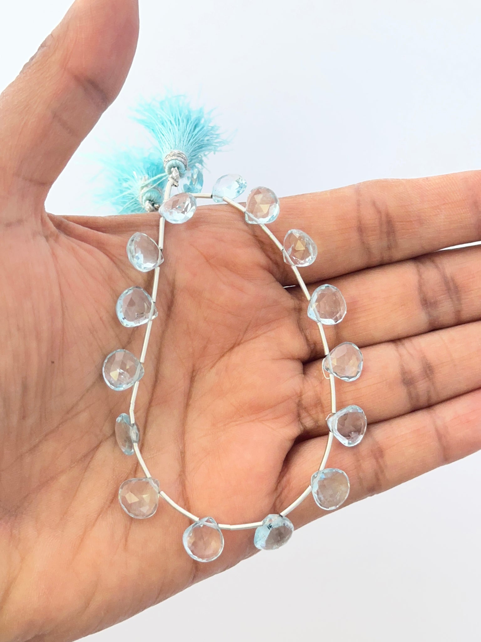 A person holds delicate strands of Sky Blue Topaz beads, showcasing their smooth design.