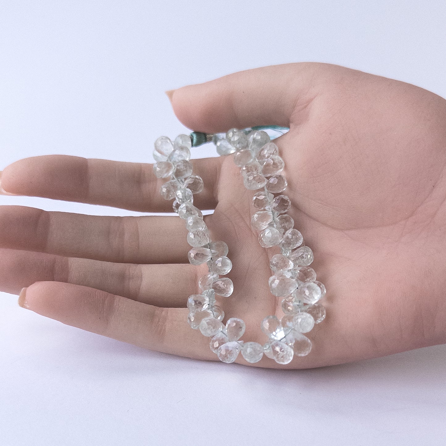 A person holds delicate strands of sky blue Topaz faceted briolette beads, showcasing their teardrop design.