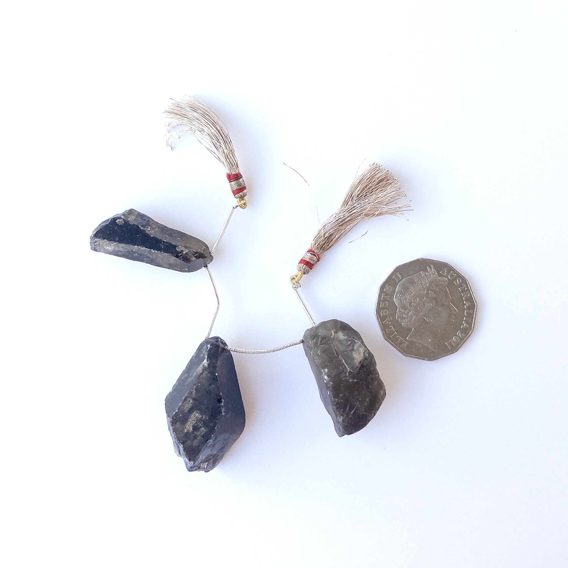 A coin is place near delicate pieces of Smoky Quartz rough beads for scale.