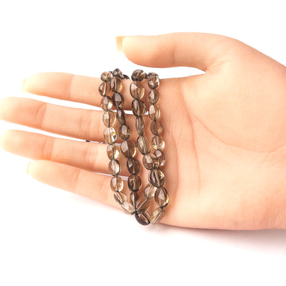 A person holds delicate strands of Smoky Quartz beads, showcasing their faceted oval design.