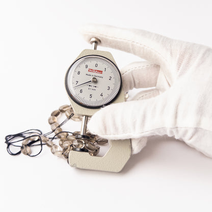 A dial gauge measures the Smoky Quartz Faceted Oval 6.5-7.5mm gemstone.