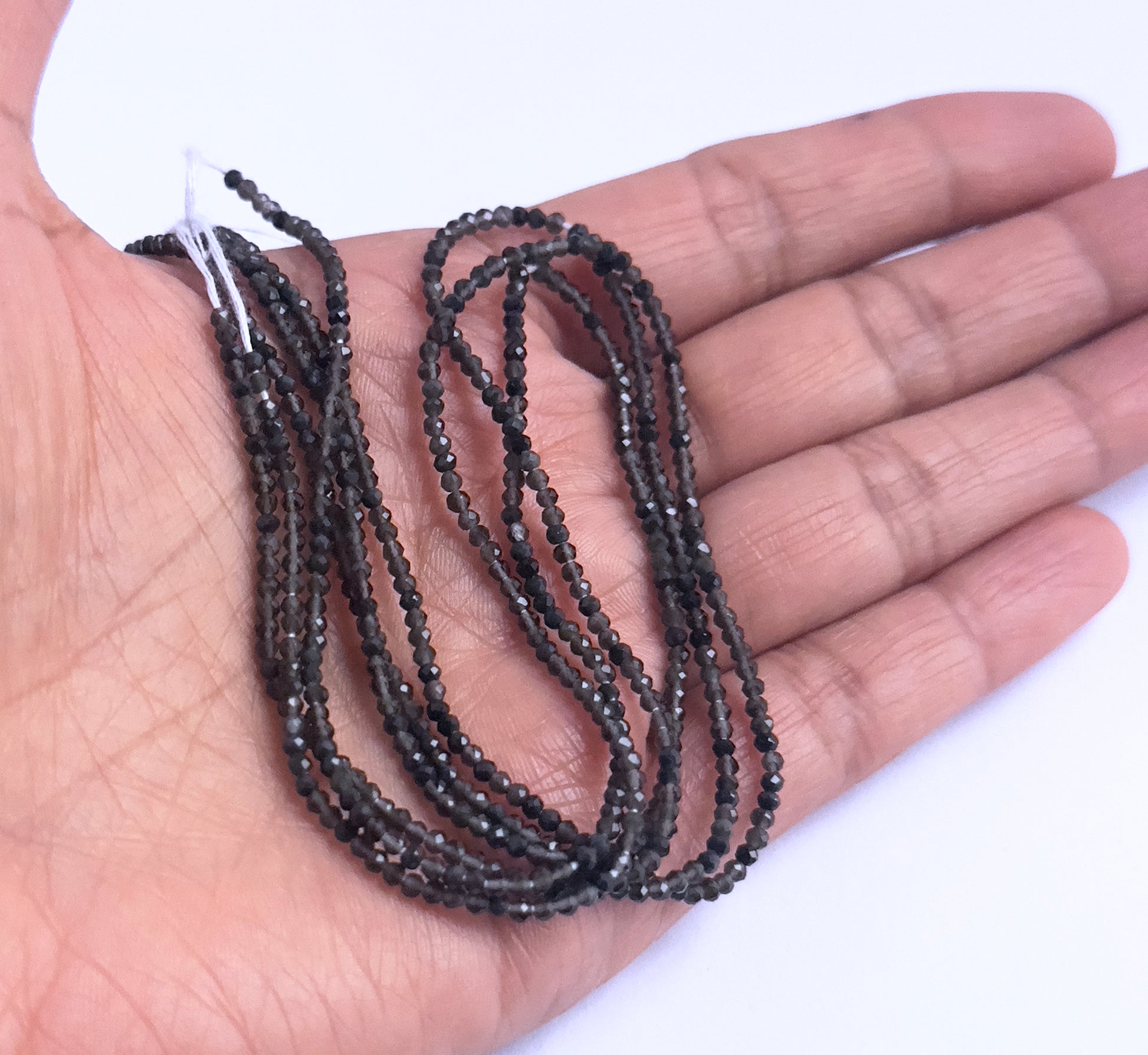 A person holds delicate strands of Smoky Quartz beads, showcasing their faceted design.