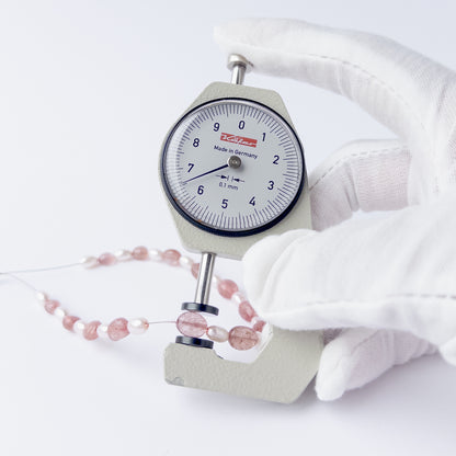 A dial gauge measures the Strawberry Quartz and Shell Pearl smooth oval 5–7mm gemstone.