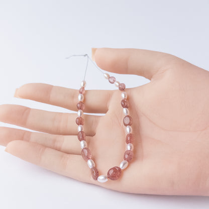 A person holds delicate strands of Strawberry Quartz and Shell Pearl beads, showcasing their smooth oval design.
