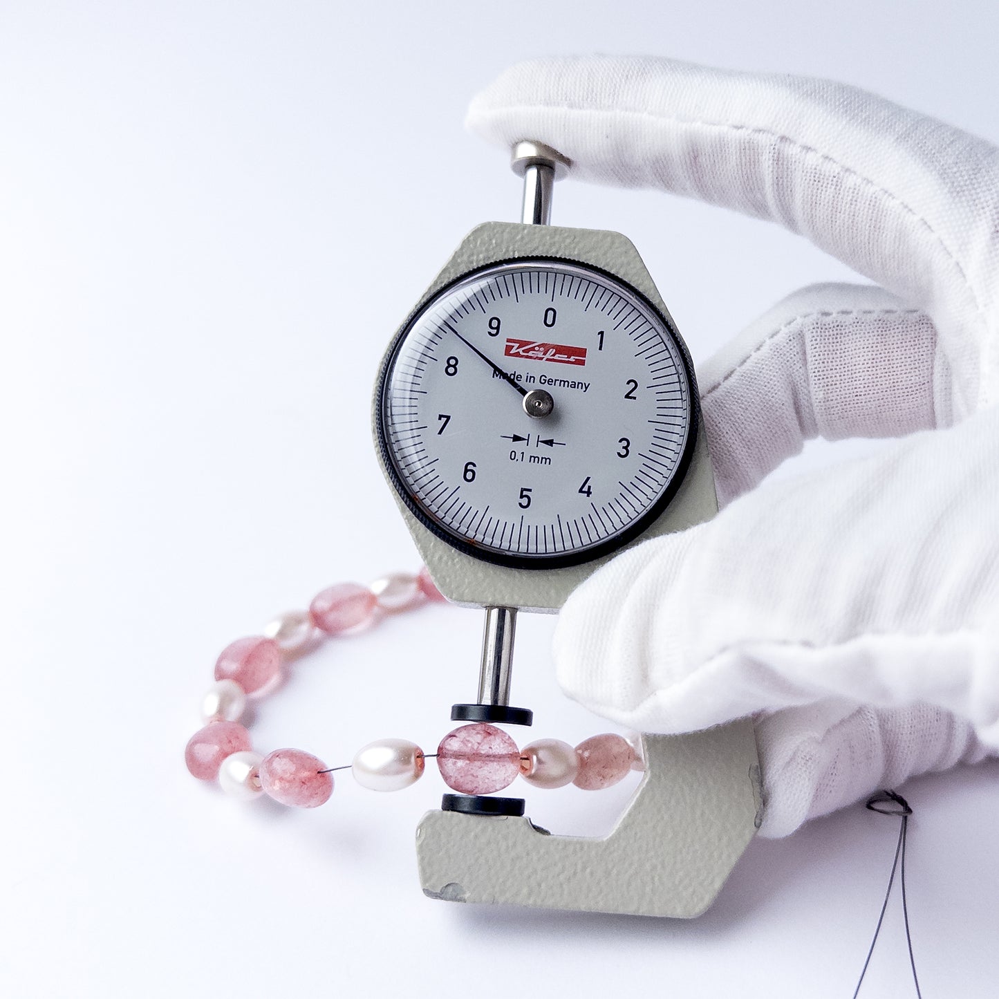 A dial gauge measures the Strawberry Quartz and Shell Pearl smooth oval 6.7–8.5mm gemstone.
