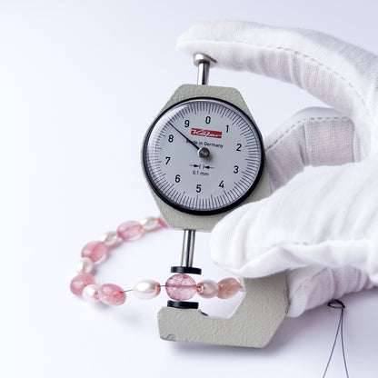 A dial gauge measures the Strawberry Quartz and Shell Pearl smooth oval 6.7–8.5mm gemstone.